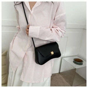 Close-up of black leather baguette bag with gold metal buckle and thin shoulder strap