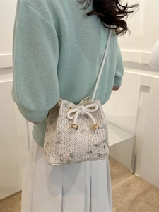 Woven straw bucket bag with floral embroidery and drawstring closure shown on model