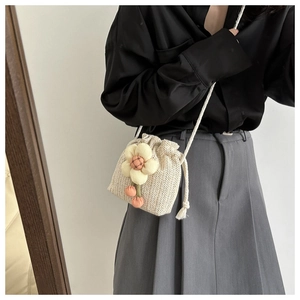 Close-up of mini straw crossbody bag with floral applique and pink pompom charms
