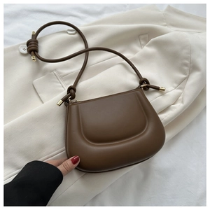 Detail of dark brown puffer saddle bag with knotted strap on a white blazer