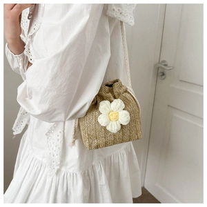 Detail view of woven straw bucket bag with large white crochet flower and drawstring strap