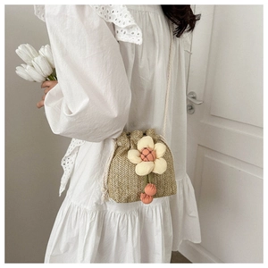 Detail of mini straw bucket bag featuring a large fabric flower and pink pompom charms