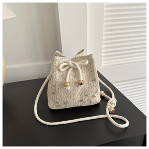 Sac seau tissé beige avec broderie florale et cordon de serrage sur une table noire