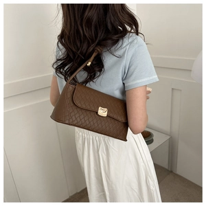 Detail of a brown quilted shoulder bag with a gold curved buckle and metallic sphere strap