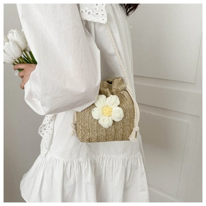 Detailed shot of woven straw bucket bag with white knit flower and slim strap