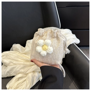 Detail of hand-woven cream bucket bag featuring a large crochet flower and drawstring closure