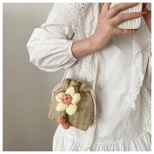 Detail of straw woven bucket bag featuring plush sunflower and white drawstring closure