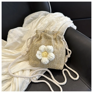 Detail of woven straw bucket bag featuring white knit daisy decor and cotton drawstring strap