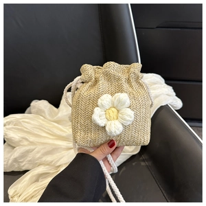 Detail of beige straw bucket bag with knitted white flower and drawstring closure