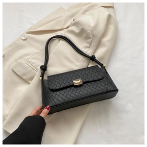 Detailed macro view of black quilted faux leather bag with gold hardware on a beige blazer