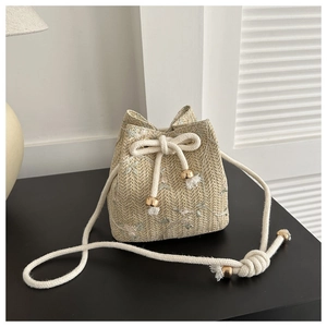 Détail du sac seau en paille avec broderie florale, cordon de serrage et perles dorées