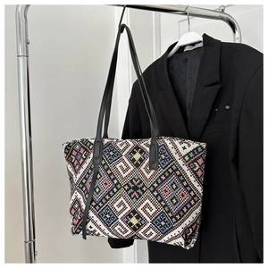 Close-up of woven ethnic geometric patterns and black leather straps on a tote bag