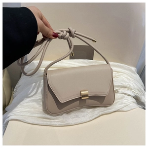 Close-up of beige leather crossbody bag with curved base and golden metal magnetic buckle