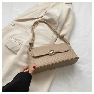 Detail of beige quilted baguette bag featuring a gold U-shaped buckle and knotted strap