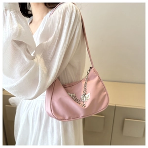 Pink shoulder bag with silver butterfly chain detail shown on a model in white dress