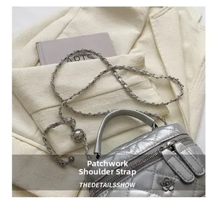Detail of silver quilted bucket bag featuring a flower zipper pull and chain strap