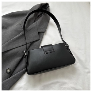 Close-up of a minimalist black rectangle shoulder bag paired with a grey office blazer