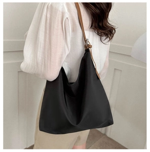 Detail of a large black tote bag with brown leather straps worn by a model