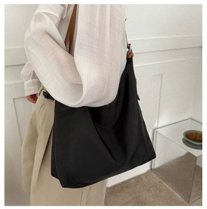 Detail view of large black canvas tote bag with brown leather straps on model shoulder