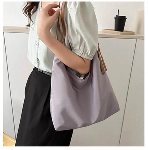 Detail view of purple canvas tote bag with brown leather straps worn by a model