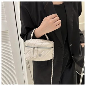 Close-up of a white quilted mini bucket bag featuring a silver metal camellia flower detail