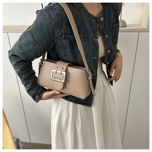 Close-up of beige underarm bag with large silver buckle on a stylish model