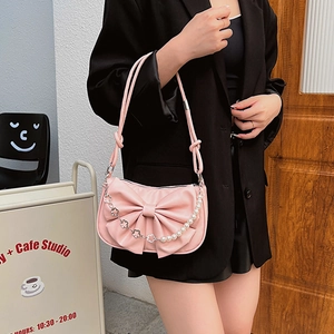 Pink bow underarm bag with pearl chain and floral metal accents in lifestyle setting