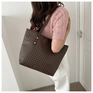 Side view of a large brown monogram tote bag with leather straps on model shoulder