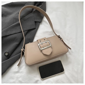 Detail of minimalist beige baguette bag with a large silver buckle and wide strap on fabric