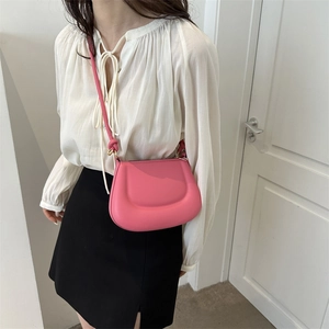 Pink saddle crossbody bag with twisted strap shown on model against a white wall