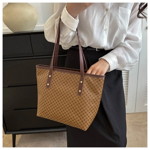 Detail of a brown polka dot tote bag with leather handles and gold rivet accents
