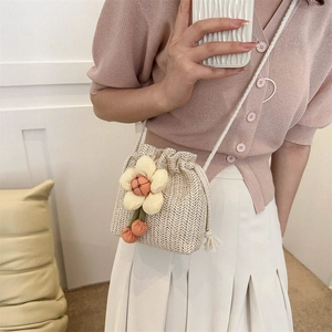 Handwoven straw bucket bag with floral charm and drawstring closure on a model