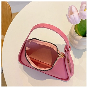 Dettaglio della borsa rosa in finta pelle con cuciture e tracolla su un tavolo bianco
