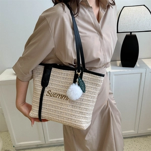 Straw woven tote bag with black leather straps and decorative pom pom charm