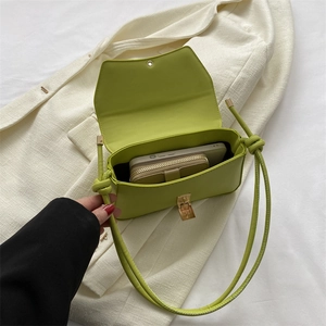 Lime green minimalist baguette bag on beige blazer featuring gold buckle and knot strap