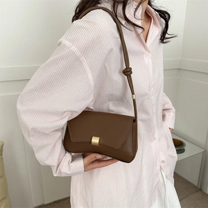 Brown leather baguette bag with asymmetrical flap and gold buckle on striped shirt