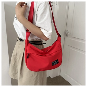 Dettaglio della borsa a mezzaluna in nylon rosso con tracolla larga e logo applicato