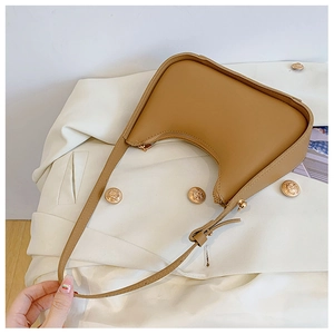 Borsa sottobraccio in pelle caramello su un blazer bianco con bottoni dorati di lusso