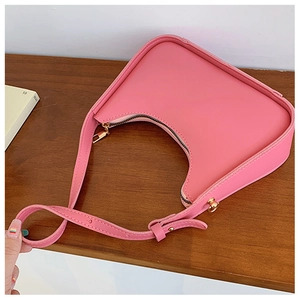 Dettaglio di una borsa a tracolla a mezzaluna in pelle rosa opaca con finiture dorate su legno