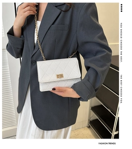 Detail of white quilted crossbody bag with gold chain strap and turn-lock on grey blazer