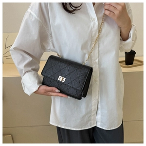 Detail of black quilted leather crossbody bag with gold metal lock and chain strap