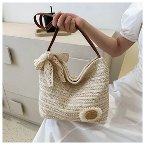 Gros plan du sac cabas en paille tissée avec nœud en dentelle et charm fleuri