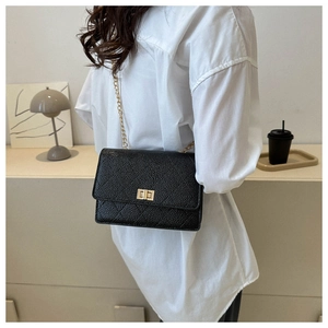 Detail of a black lychee texture flap bag with golden chain strap and swivel lock closure