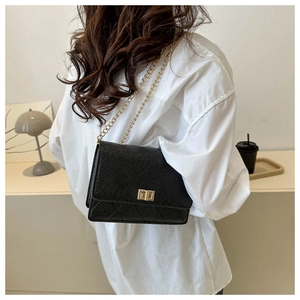 Lifestyle view of a black quilted crossbody bag with gold chain and square lock on model