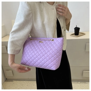 Detail of purple quilted shoulder bag with gold chain strap worn by a model