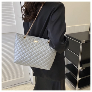 Close-up of light grey quilted tote bag with golden chain straps and embroidery
