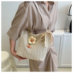 Détail du sac seau en paille tressée avec applique florale et nœud en dentelle