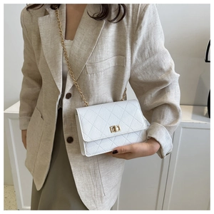 Close-up of white quilted crossbody bag with gold chain strap worn on beige blazer