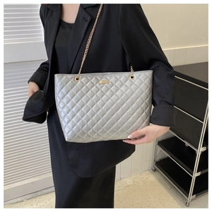 Detail of grey quilted tote bag with gold chain strap worn with a black blazer