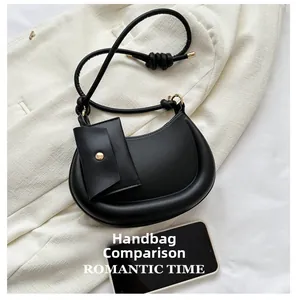 Top view of black crescent bag with knotted strap and mini pouch next to a smartphone